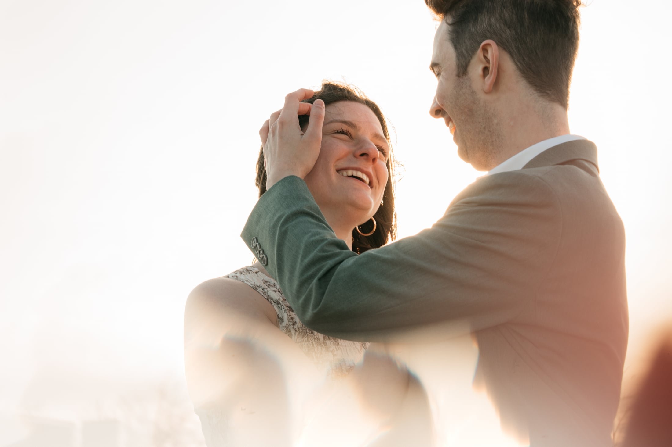 Tim brushes a strand of hair from Hanna's cheek as she laughs up at him, both lit by a hazy golden sunset
